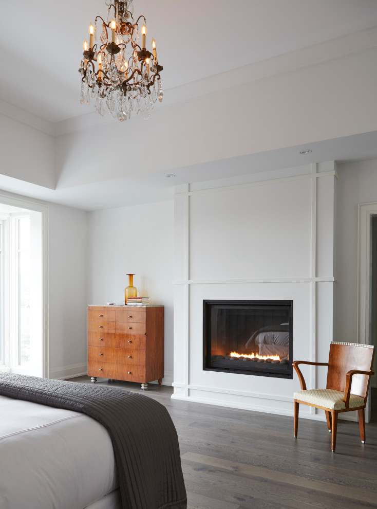 Photo of a large contemporary master bedroom in Toronto with white walls, dark hardwood floors, a standard fireplace, a plaster fireplace surround and brown floor.