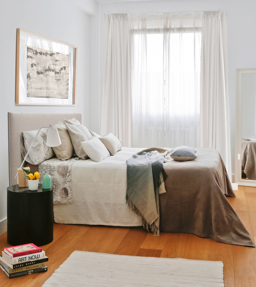 Small contemporary master bedroom in Madrid with white walls, medium hardwood floors, no fireplace and orange floor.