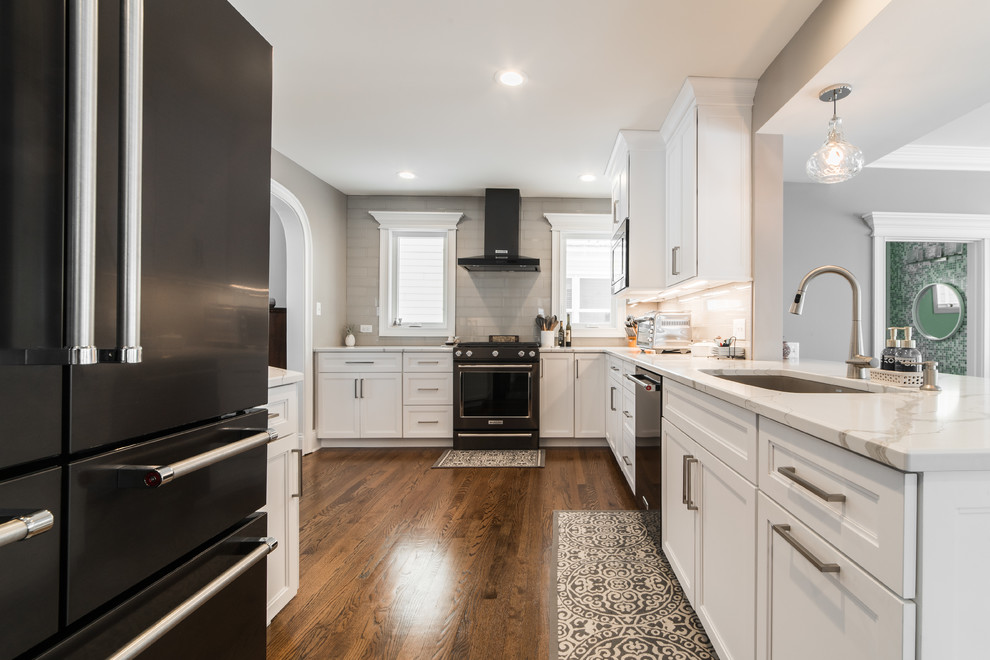 Inspiration for a mid-sized transitional l-shaped medium tone wood floor and brown floor eat-in kitchen remodel in Chicago with an undermount sink, recessed-panel cabinets, white cabinets, quartzite countertops, gray backsplash, subway tile backsplash, black appliances, no island and multicolored countertops