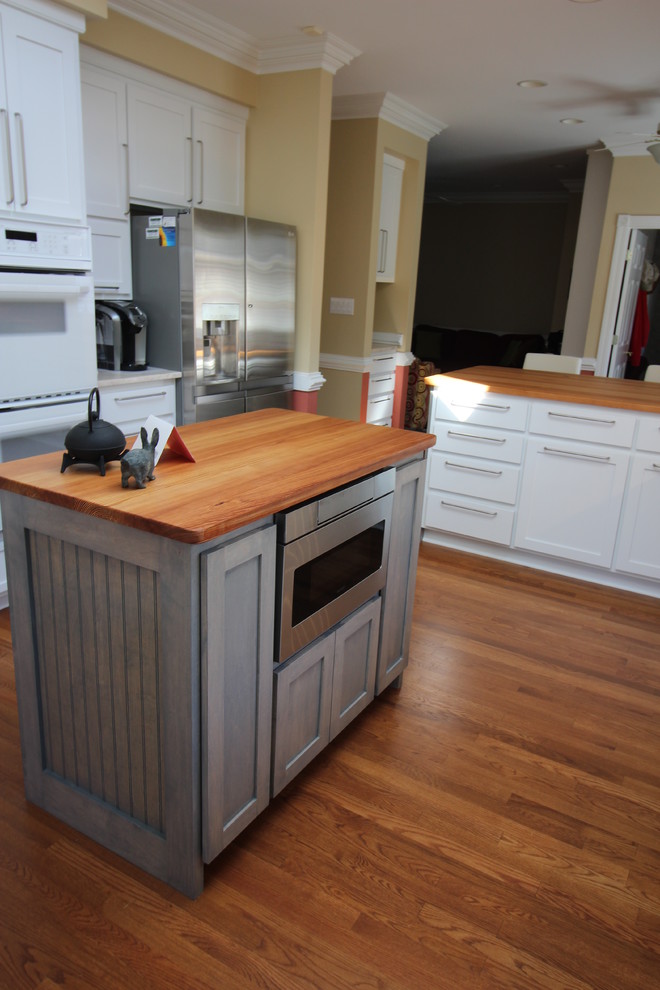 Eat-in kitchen - mid-sized transitional u-shaped medium tone wood floor eat-in kitchen idea with a farmhouse sink, shaker cabinets, yellow cabinets, marble countertops, beige backsplash, stone tile backsplash, stainless steel appliances and an island