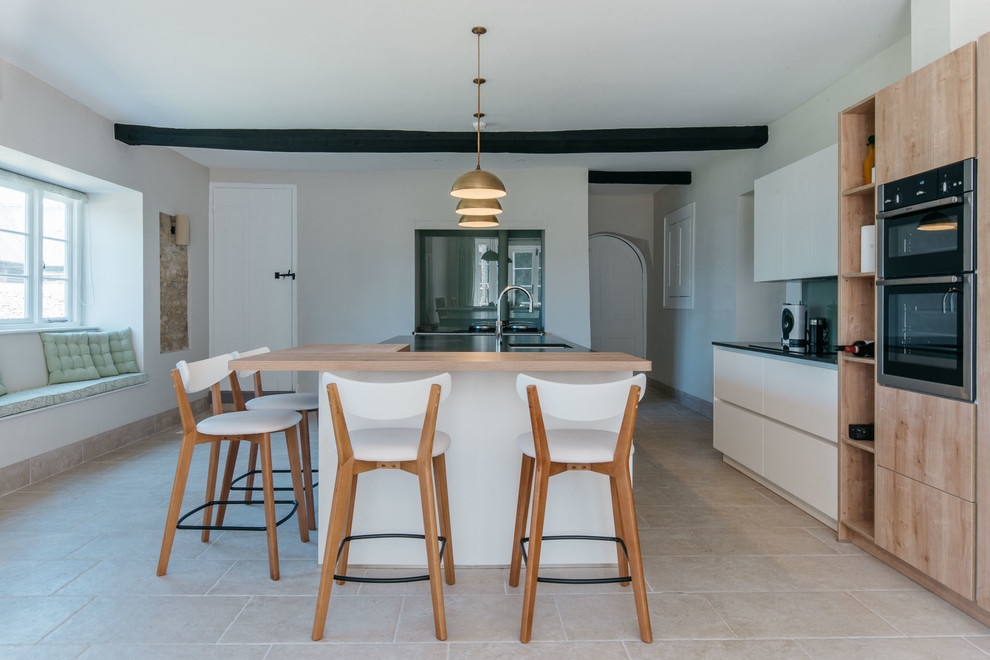 Large contemporary galley eat-in kitchen in Oxfordshire with flat-panel cabinets, granite benchtops, green splashback, glass sheet splashback, coloured appliances, ceramic floors, with island, beige floor, black benchtop, an undermount sink and light wood cabinets.