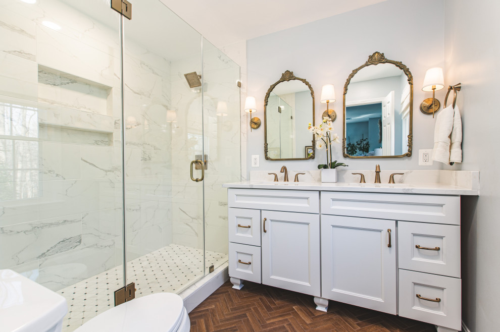 This is an example of a mid-sized transitional master wet room bathroom in DC Metro with furniture-like cabinets, white cabinets, an alcove tub, a one-piece toilet, gray tile, ceramic tile, grey walls, wood-look tile, an undermount sink, engineered quartz benchtops, brown floor, a hinged shower door, white benchtops, a shower seat, a double vanity and a built-in vanity.
