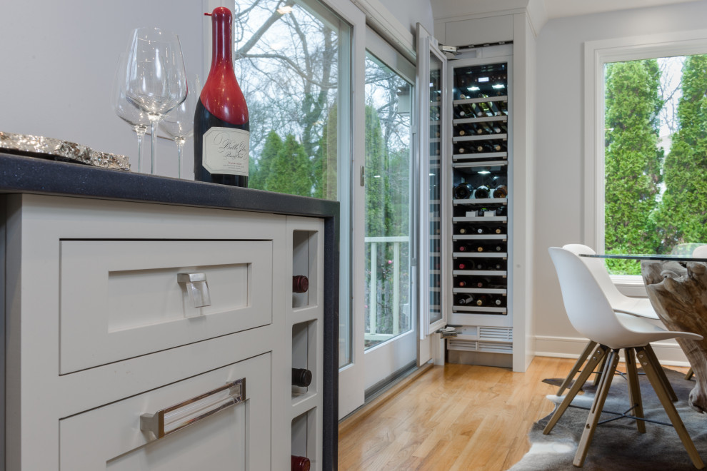 Photo of a mid-sized contemporary galley wet bar in New York with an undermount sink, recessed-panel cabinets, white cabinets, quartz benchtops, white splashback, glass tile splashback, light hardwood floors, beige floor and beige benchtop.
