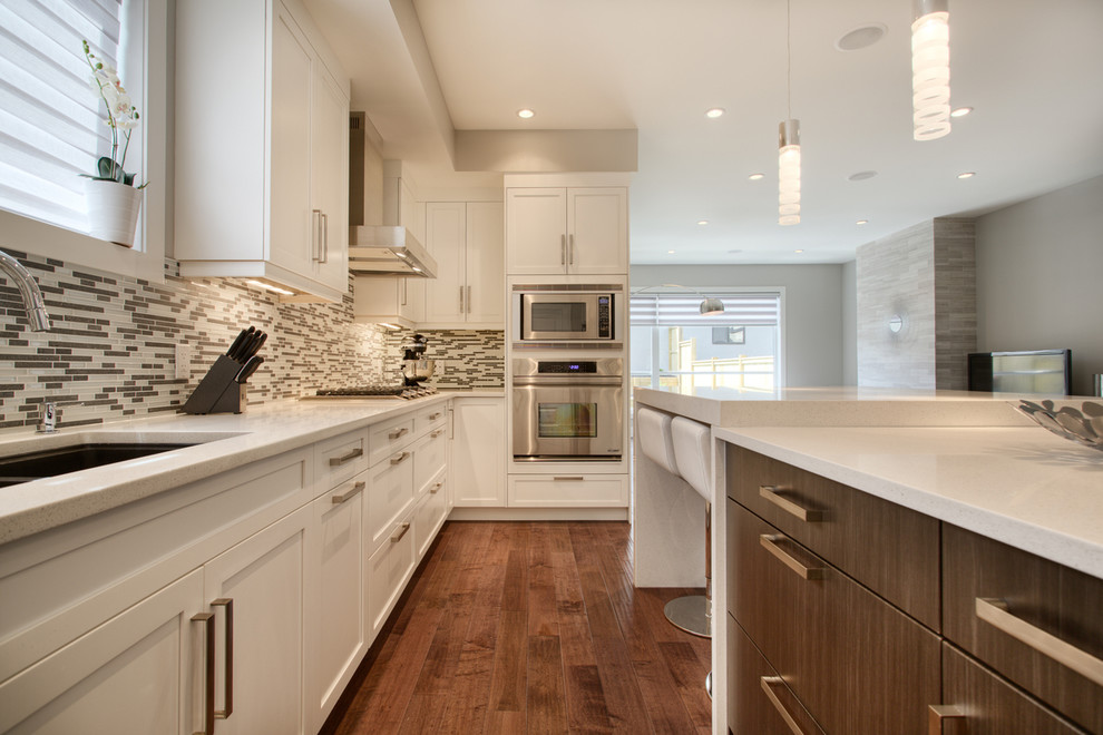 Contemporary kitchen in Calgary with an undermount sink, shaker cabinets, white cabinets, matchstick tile splashback and stainless steel appliances.