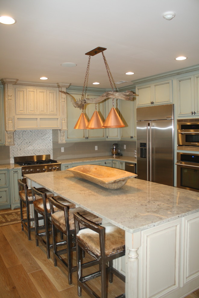 Large mountain style u-shaped light wood floor eat-in kitchen photo with a farmhouse sink, raised-panel cabinets, green cabinets, granite countertops, gray backsplash, ceramic backsplash, stainless steel appliances and an island