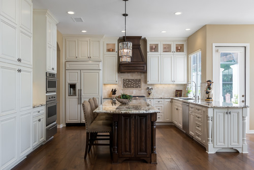 Traditional kitchen with cream raised-panel cabinet doors, crown moulding, dark wood island, granite countertops, and a decorative range hood