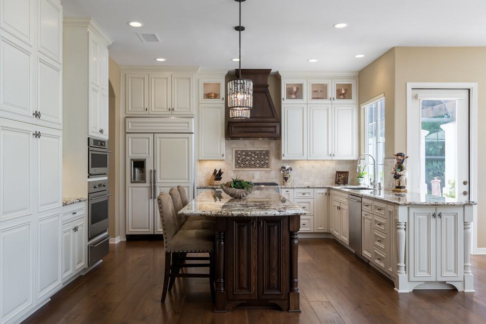 Inspiration for a traditional l-shaped kitchen in San Diego with raised-panel cabinets, white cabinets, granite benchtops, beige splashback, stainless steel appliances, dark hardwood floors, with island and brown floor.