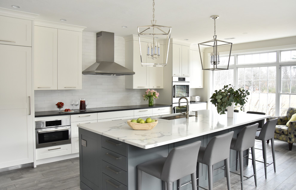 Design ideas for a transitional kitchen in Boston with white splashback, marble splashback, grey floor, an undermount sink, shaker cabinets, white cabinets, stainless steel appliances, with island and white benchtop.