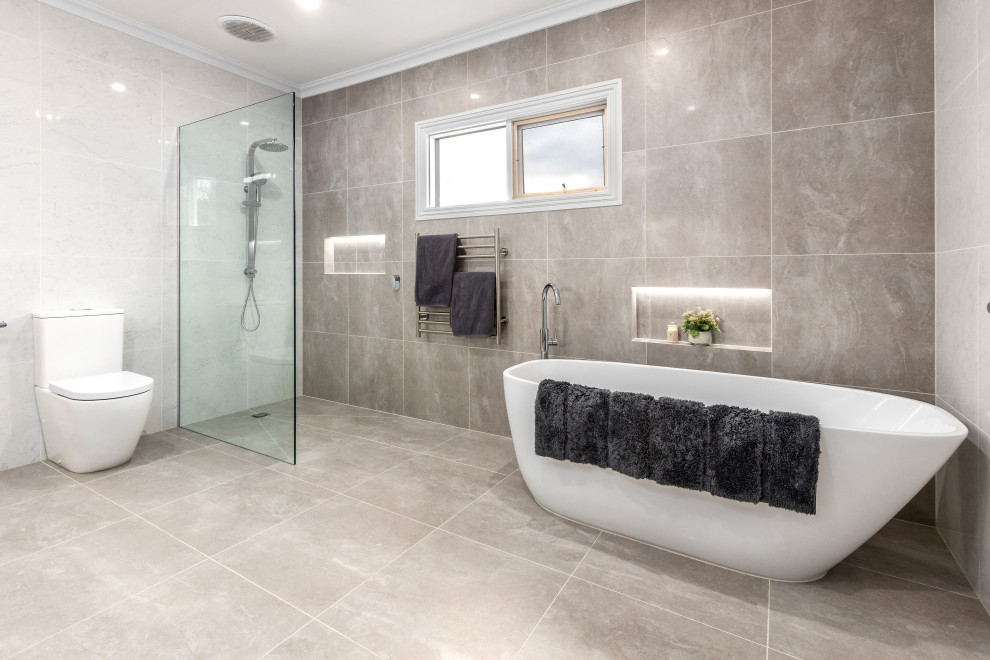 This is an example of a mid-sized contemporary master bathroom in Melbourne with flat-panel cabinets, light wood cabinets, a freestanding tub, an open shower, a wall-mount toilet, white tile, porcelain tile, grey walls, porcelain floors, a drop-in sink, engineered quartz benchtops, beige floor, an open shower, brown benchtops, a niche, a double vanity and a built-in vanity.