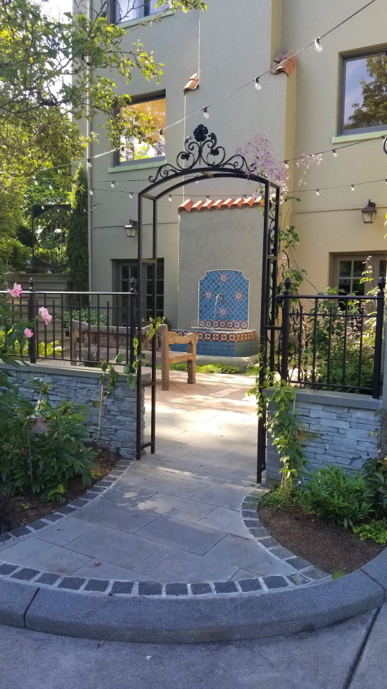 This is an example of a mediterranean courtyard formal partial sun garden for summer in Seattle with a water feature, natural stone paving and a metal fence.