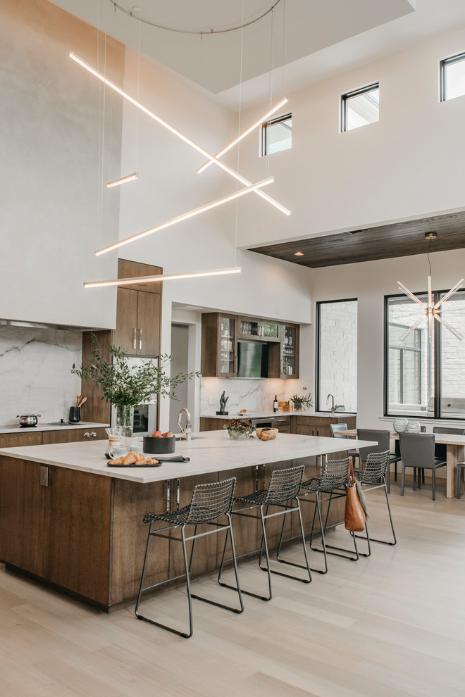 Expansive contemporary l-shaped eat-in kitchen in Austin with a single-bowl sink, flat-panel cabinets, medium wood cabinets, quartzite benchtops, white splashback, stone slab splashback, stainless steel appliances, light hardwood floors, with island and white benchtop.