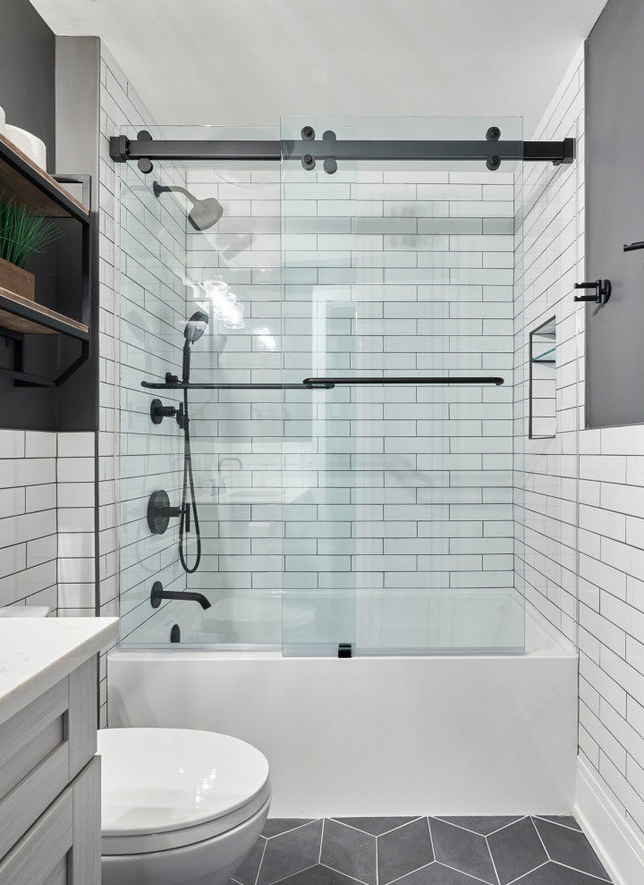 This is an example of a mid-sized transitional kids bathroom in Chicago with recessed-panel cabinets, grey cabinets, an alcove tub, a shower/bathtub combo, gray tile, porcelain tile, white walls, porcelain floors, quartzite benchtops, grey floor, a sliding shower screen, white benchtops, a niche, a single vanity and a freestanding vanity.