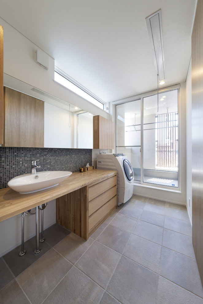 Industrial laundry room in Yokohama with flat-panel cabinets, light wood cabinets, wood benchtops, white walls, grey floor and an integrated washer and dryer.