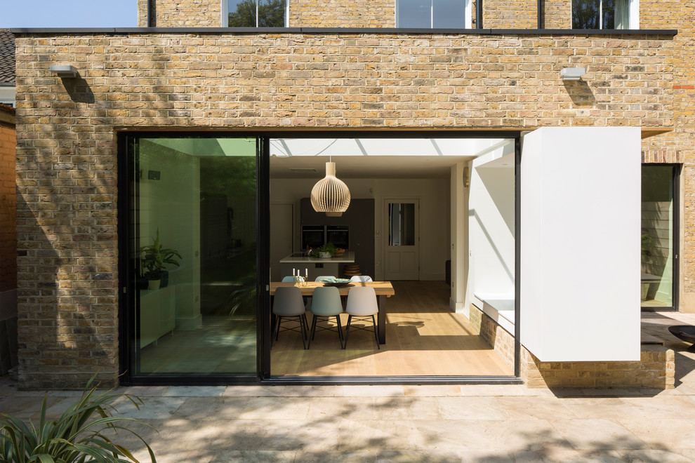 This is an example of a contemporary three-storey brick yellow house exterior in London with a mixed roof.