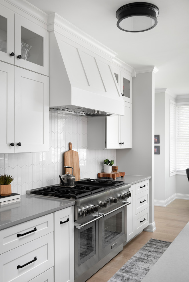 Open concept kitchen - mid-sized transitional galley light wood floor open concept kitchen idea in Chicago with an undermount sink, shaker cabinets, white cabinets, quartz countertops, white backsplash, ceramic backsplash, stainless steel appliances, an island and gray countertops