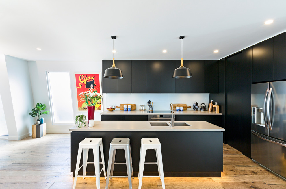 Contemporary kitchen in Melbourne with a double-bowl sink, flat-panel cabinets, black cabinets, white splashback, stainless steel appliances, light hardwood floors and with island.
