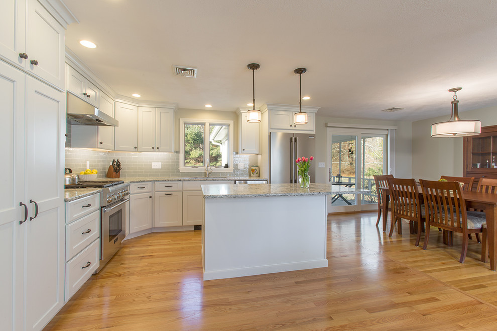 Mid-sized transitional l-shaped medium tone wood floor eat-in kitchen photo in Boston with an undermount sink, recessed-panel cabinets, white cabinets, quartz countertops, green backsplash, ceramic backsplash, stainless steel appliances and an island