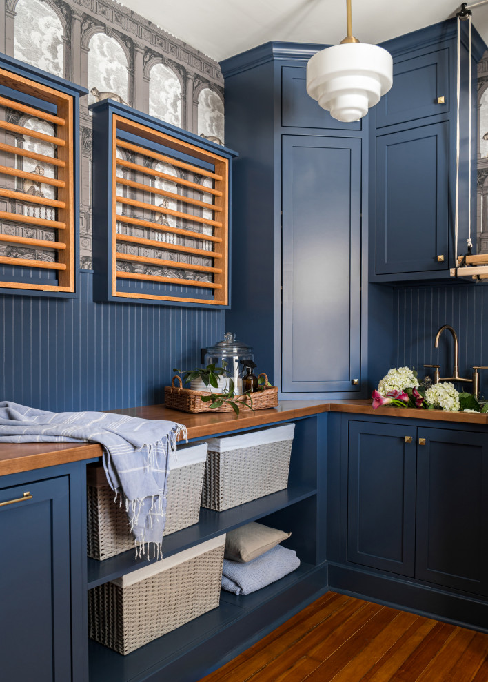 Inspiration for a large transitional u-shaped dedicated laundry room in Chicago with an undermount sink, shaker cabinets, blue cabinets, wood benchtops, blue splashback, shiplap splashback, white walls, dark hardwood floors, a side-by-side washer and dryer, brown floor, brown benchtop and wallpaper.
