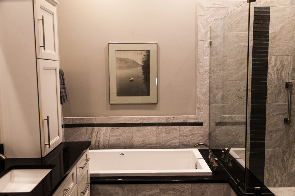 Transitional master gray tile and ceramic tile double-sink drop-in bathtub photo with a two-piece toilet, gray walls, an undermount sink, quartzite countertops, a hinged shower door and black countertops