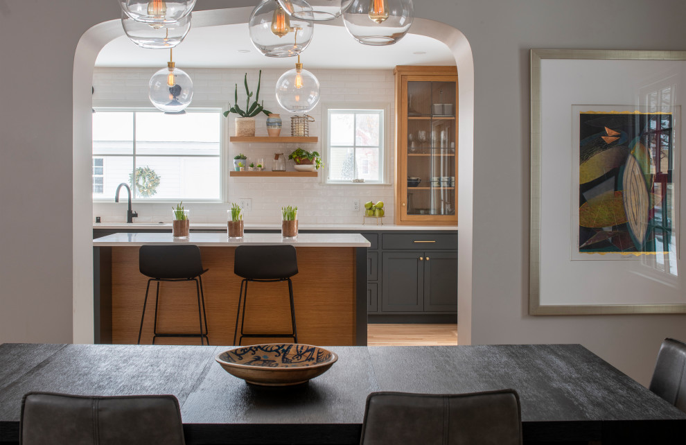 Mid-sized transitional l-shaped kitchen in Minneapolis with an undermount sink, flat-panel cabinets, medium wood cabinets, solid surface benchtops, white splashback, ceramic splashback, stainless steel appliances, light hardwood floors, with island and white benchtop.