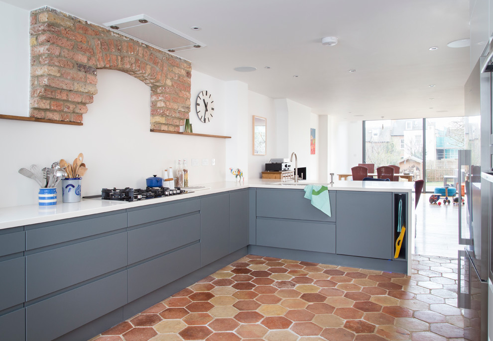 Large contemporary l-shaped eat-in kitchen in London with a double-bowl sink, flat-panel cabinets, blue cabinets, solid surface benchtops, white splashback, stainless steel appliances, terra-cotta floors, with island, multi-coloured floor and white benchtop.