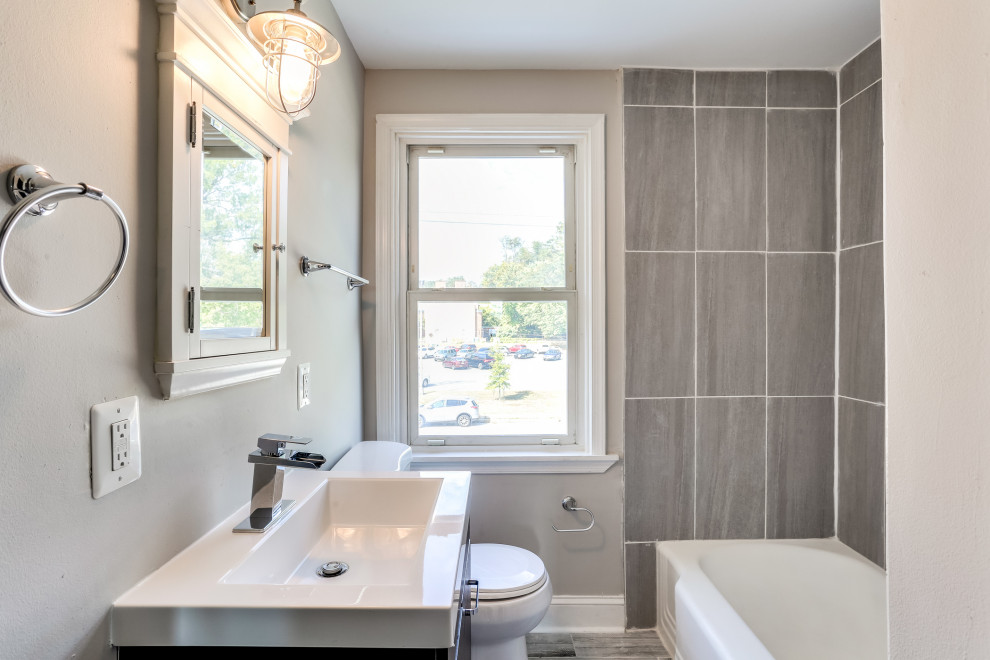 This is an example of a small traditional family bathroom in Baltimore with shaker cabinets, brown cabinets, a corner bath, a one-piece toilet, grey tiles, ceramic tiles, grey walls, laminate floors, a built-in sink, solid surface worktops, grey floors, white worktops, a single sink and a built in vanity unit.