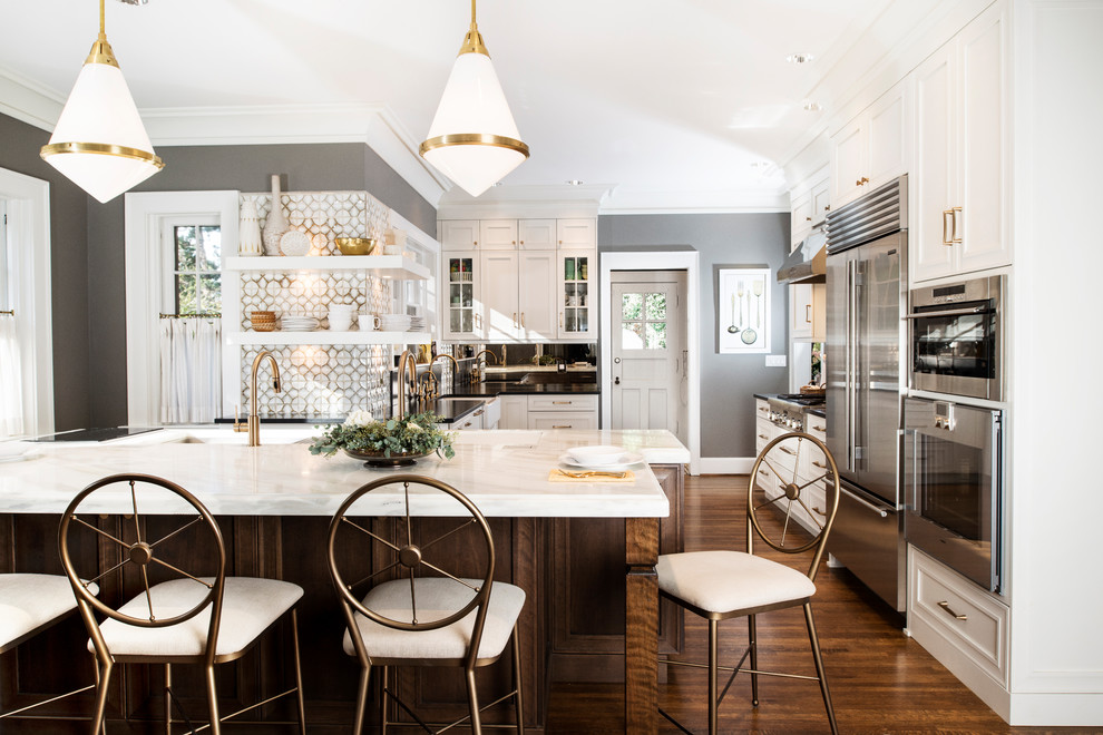 This is an example of a large transitional u-shaped eat-in kitchen in Other with marble benchtops, white splashback, glass tile splashback, stainless steel appliances, medium hardwood floors, with island, brown floor, a farmhouse sink, recessed-panel cabinets and white cabinets.