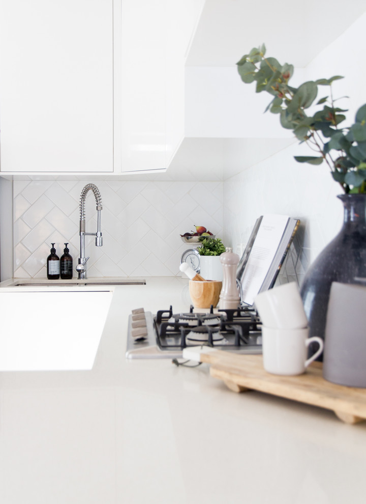 This is an example of a scandinavian u-shaped open plan kitchen in Sydney with an undermount sink, flat-panel cabinets, white cabinets, white splashback, porcelain splashback, stainless steel appliances, light hardwood floors and no island.