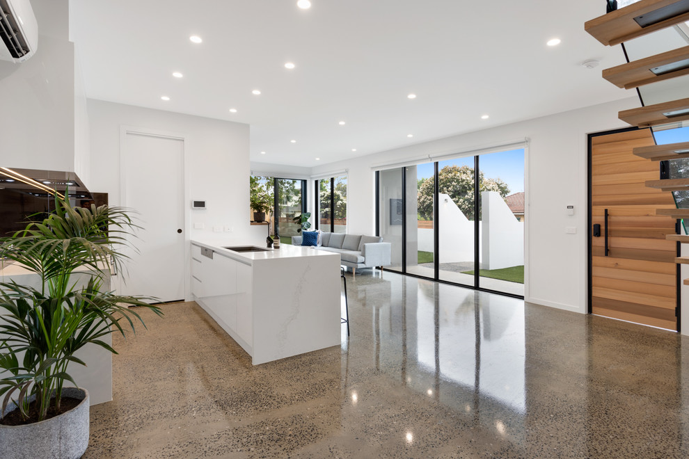 Mid-sized contemporary galley open plan kitchen in Melbourne with an undermount sink, white cabinets, granite benchtops, concrete floors, with island, grey floor and white benchtop.