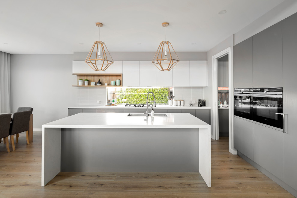 Large contemporary l-shaped kitchen in Melbourne with an undermount sink, flat-panel cabinets, grey cabinets, white splashback, porcelain splashback, panelled appliances, with island, beige floor and white benchtop.