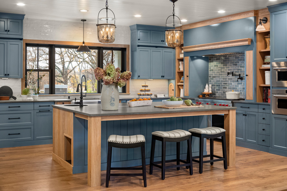 Large beach style u-shaped kitchen in Minneapolis with a farmhouse sink, recessed-panel cabinets, blue cabinets, quartzite benchtops, grey splashback, ceramic splashback, stainless steel appliances, medium hardwood floors, with island, brown floor, grey benchtop and timber.