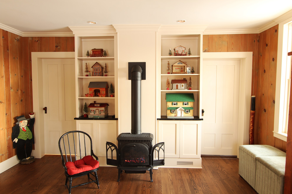 Photo of a small traditional enclosed family room in Other with brown walls, medium hardwood floors, a wood stove, a plaster fireplace surround, no tv and brown floor.
