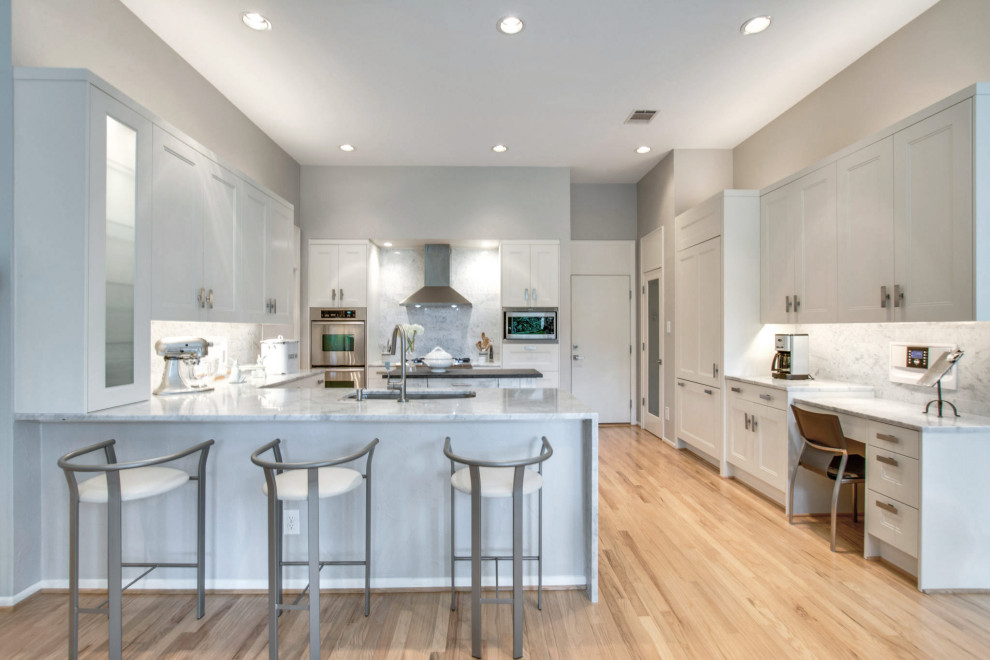 Photo of a large modern u-shaped eat-in kitchen with a single-bowl sink, shaker cabinets, white cabinets, marble benchtops, white splashback, marble splashback, stainless steel appliances, light hardwood floors, with island, beige floor and white benchtop.
