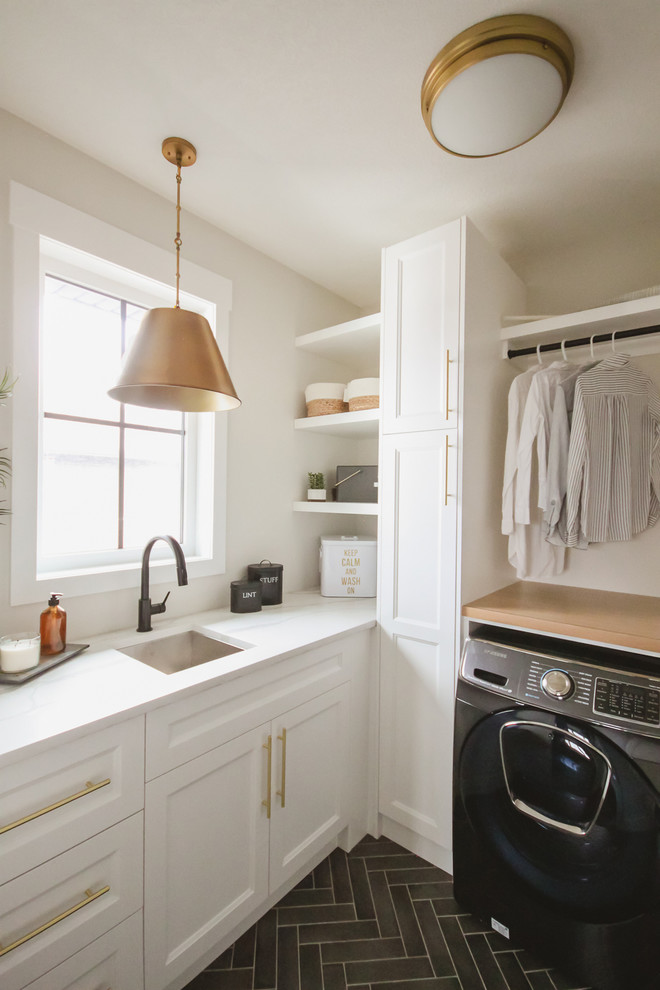 Photo of a transitional l-shaped laundry room in Other with an undermount sink, recessed-panel cabinets, white cabinets, white walls, a side-by-side washer and dryer, black floor and white benchtop.