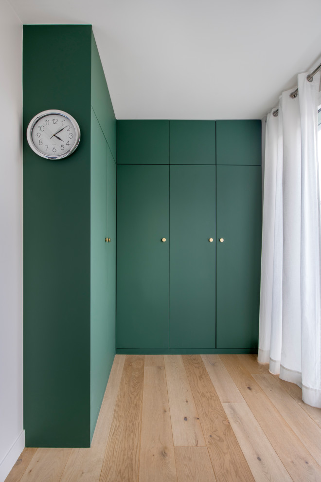 This is an example of a mid-sized modern gender-neutral dressing room in Paris with beaded inset cabinets, green cabinets, light hardwood floors and beige floor.