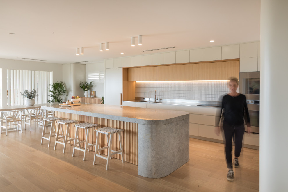 Photo of a large contemporary galley open plan kitchen in Perth with an integrated sink, white cabinets, limestone benchtops, white splashback, cement tile splashback, panelled appliances, light hardwood floors, with island, beige floor and grey benchtop.