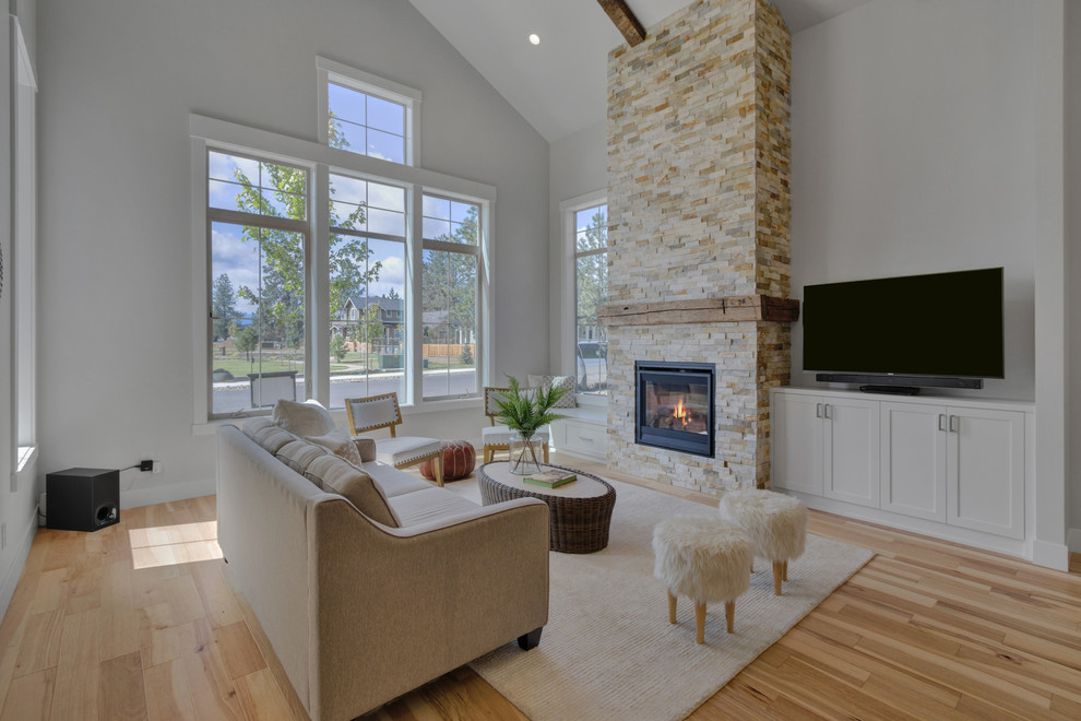 Photo of a large country open concept living room in Portland with white walls, light hardwood floors, a standard fireplace, a stone fireplace surround, a wall-mounted tv and beige floor.
