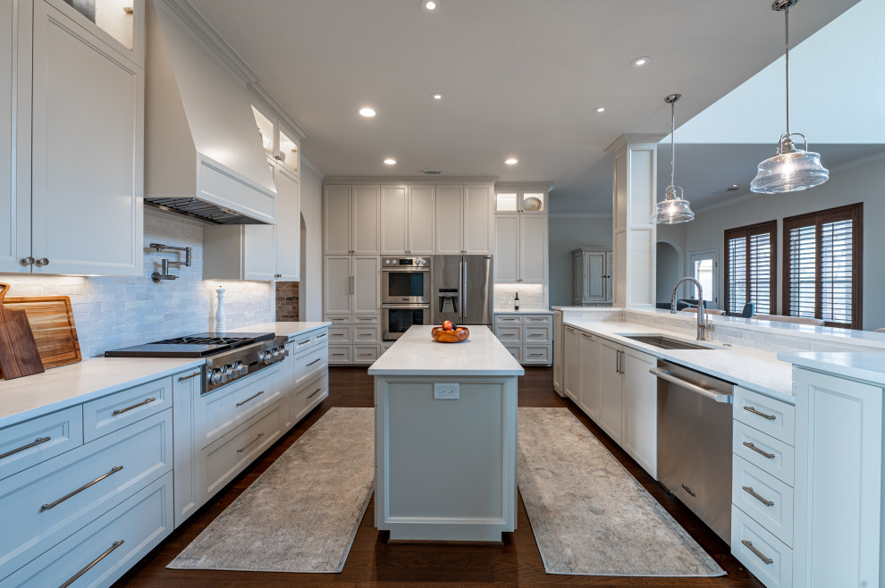 Large transitional open plan kitchen in Houston with shaker cabinets, white cabinets, granite benchtops, stone tile splashback and multiple islands.