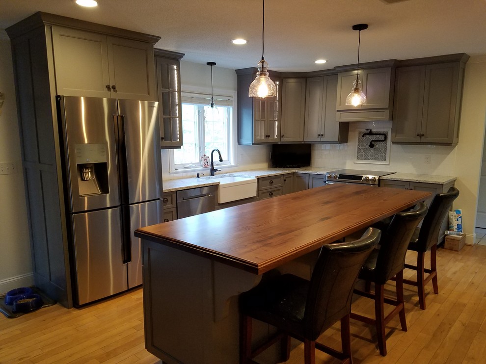 Example of a mid-sized transitional galley light wood floor and brown floor eat-in kitchen design with a farmhouse sink, recessed-panel cabinets, gray cabinets, wood countertops, white backsplash, subway tile backsplash, stainless steel appliances and an island