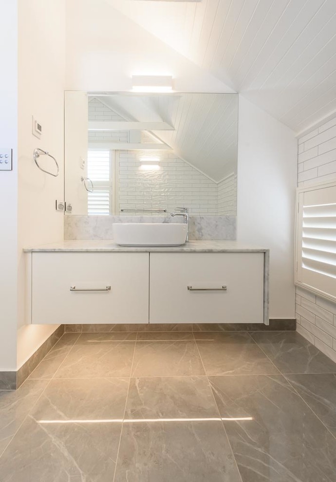 Mid-sized traditional bathroom in Melbourne with flat-panel cabinets, white cabinets, an alcove shower, a two-piece toilet, white tile, ceramic tile, white walls, porcelain floors, a vessel sink, marble benchtops, grey floor and a hinged shower door.