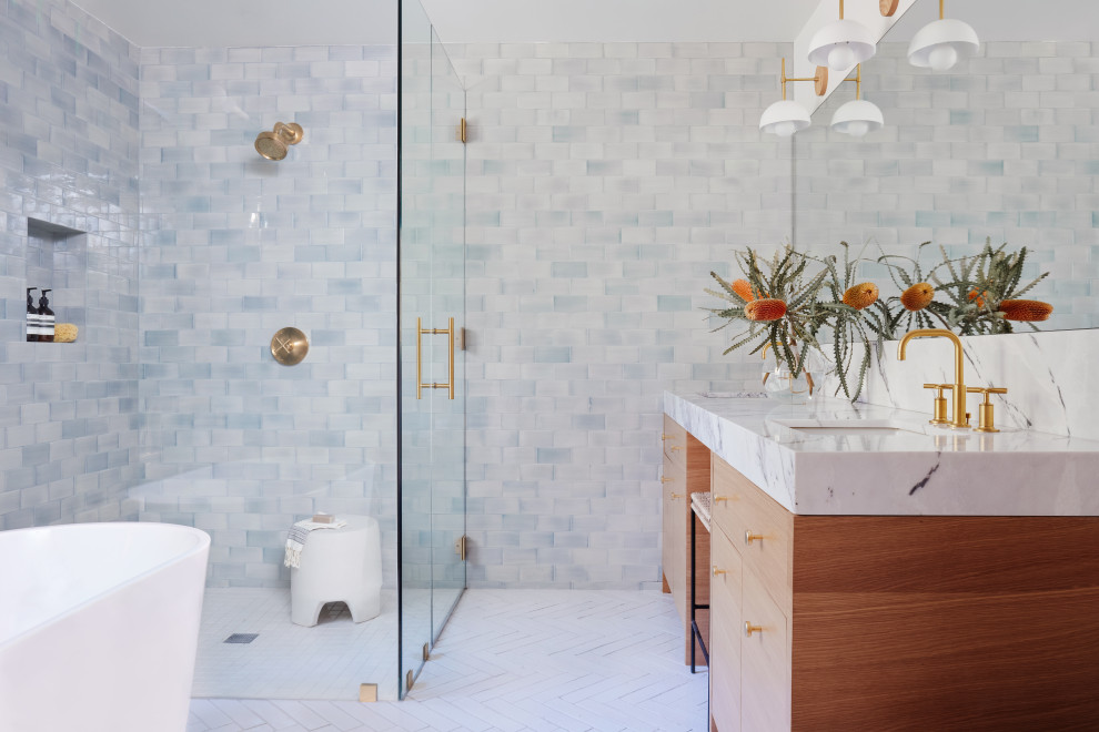 Inspiration for a medium sized ensuite bathroom in Los Angeles with flat-panel cabinets, light wood cabinets, a freestanding bath, a corner shower, a one-piece toilet, blue tiles, ceramic tiles, white walls, brick flooring, a submerged sink, marble worktops, white floors, a hinged door, white worktops, an enclosed toilet, double sinks, a built in vanity unit and wallpapered walls.