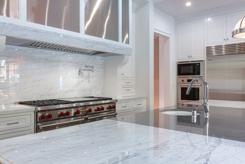 Photo of a large traditional u-shaped open plan kitchen in Los Angeles with an undermount sink, shaker cabinets, white cabinets, marble benchtops, white splashback, stone slab splashback, stainless steel appliances, with island and white benchtop.