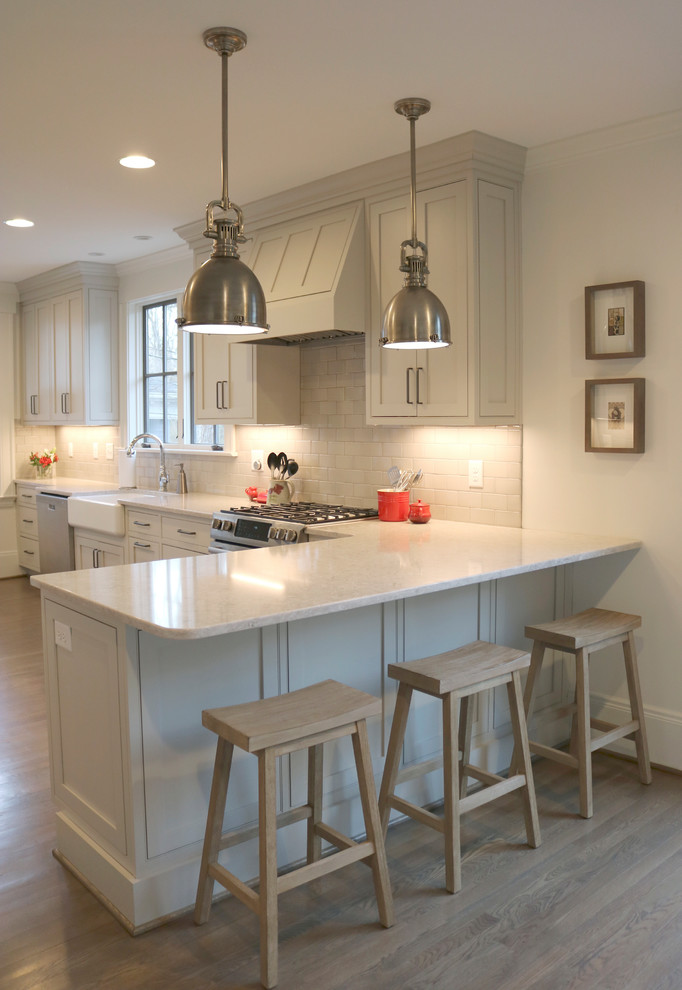 Example of a large transitional galley medium tone wood floor and brown floor enclosed kitchen design with a farmhouse sink, shaker cabinets, gray cabinets, quartzite countertops, stainless steel appliances, beige backsplash, subway tile backsplash and a peninsula
