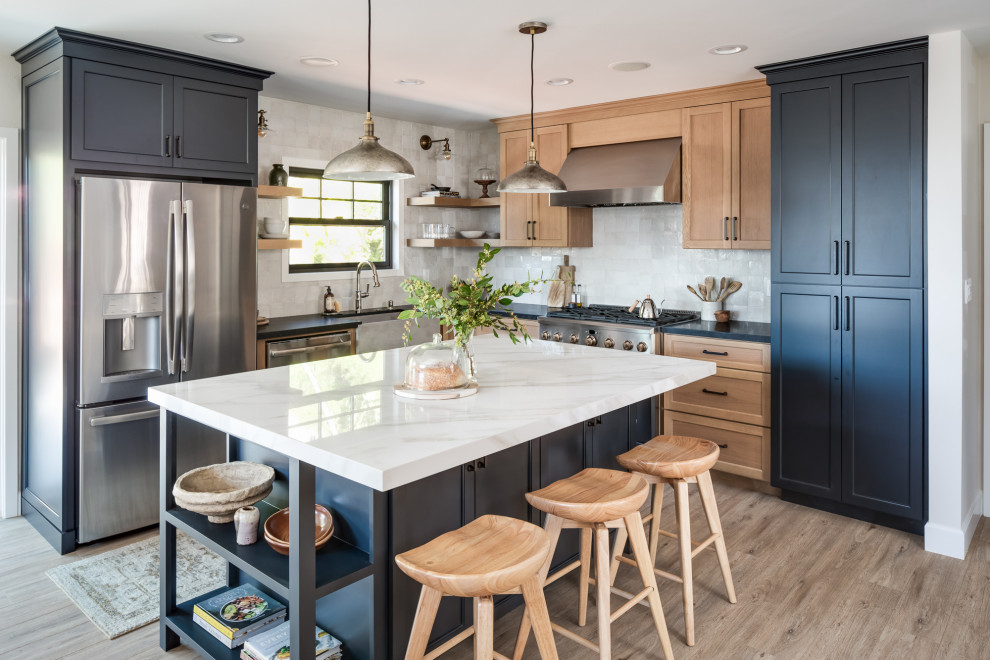 This is an example of a mid-sized transitional l-shaped kitchen in San Diego with a farmhouse sink, shaker cabinets, solid surface benchtops, white splashback, terra-cotta splashback, black appliances, vinyl floors, with island, beige floor, black benchtop and grey cabinets.