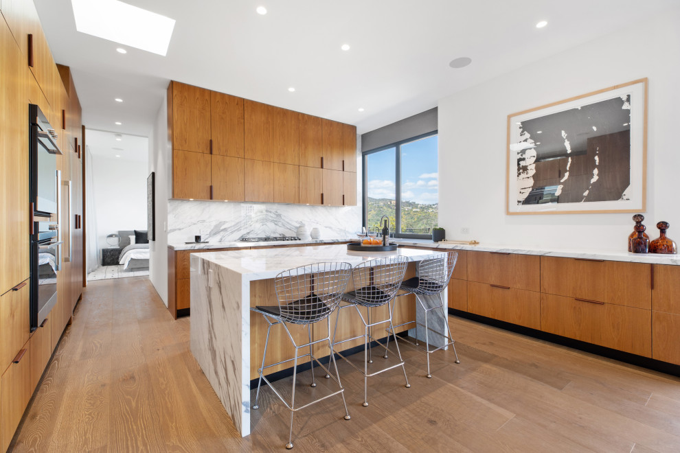 Inspiration for a large contemporary u-shaped kitchen in Los Angeles with flat-panel cabinets, medium wood cabinets, white splashback, panelled appliances, medium hardwood floors, with island, white benchtop and beige floor.