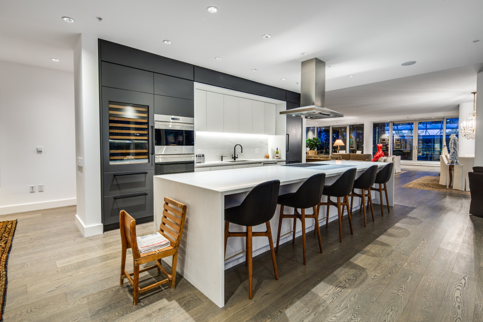 Medium sized contemporary grey and white galley kitchen/diner in Vancouver with a submerged sink, flat-panel cabinets, grey cabinets, engineered stone countertops, white splashback, engineered quartz splashback, stainless steel appliances, dark hardwood flooring, an island, brown floors and white worktops.