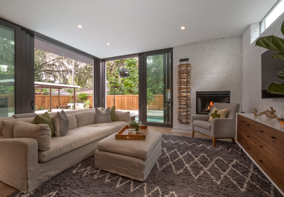 Photo of a large modern open concept living room in Austin with white walls, medium hardwood floors, a standard fireplace, a brick fireplace surround and a wall-mounted tv.