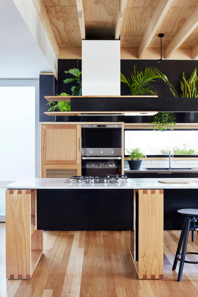 Inspiration for a small contemporary open plan kitchen in Melbourne with black cabinets, marble benchtops, white splashback, subway tile splashback, stainless steel appliances, light hardwood floors and with island.