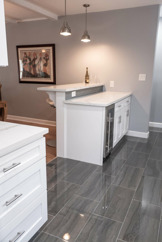 Photo of a mid-sized contemporary galley kitchen pantry in Dallas with a farmhouse sink, shaker cabinets, white cabinets, quartzite benchtops, grey splashback, ceramic splashback, white appliances, ceramic floors, a peninsula, grey floor and white benchtop.