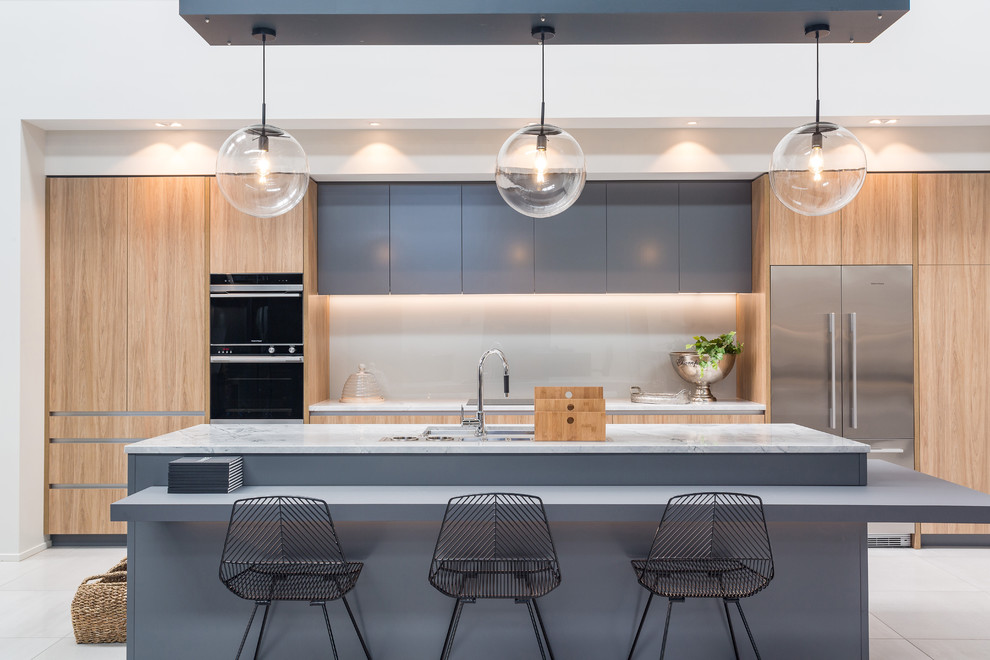 Photo of a contemporary galley kitchen in Auckland with an undermount sink, flat-panel cabinets, blue cabinets, grey splashback, glass sheet splashback, black appliances, with island and grey floor.